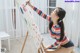 A woman is painting on an easel in a room.