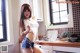 A woman in a white tank top and denim shorts posing in a kitchen.
