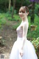 A woman in a white dress standing in the woods.