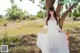 A woman in a white dress standing under a tree.