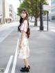 A woman in a white dress is standing on the street.